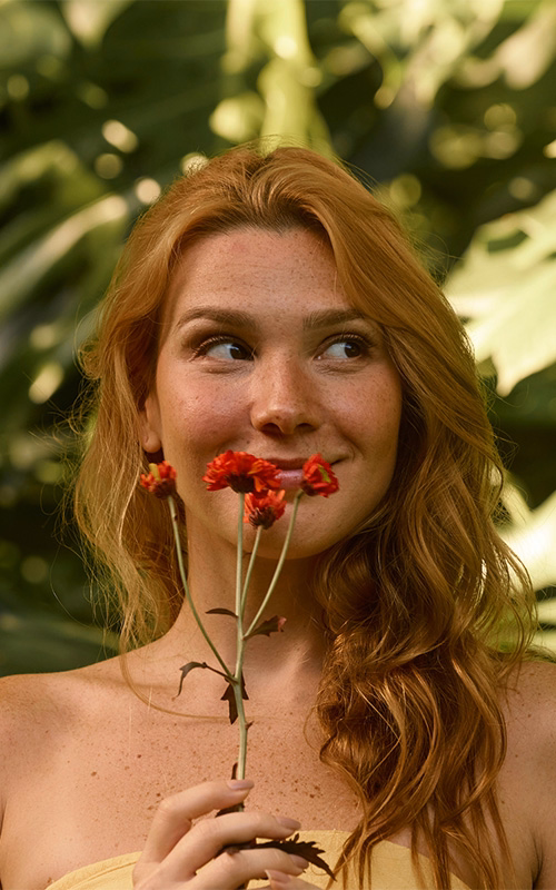 Smiling young woman with red hair holding red wildflowers outdoors, representing choosing the right birth control option