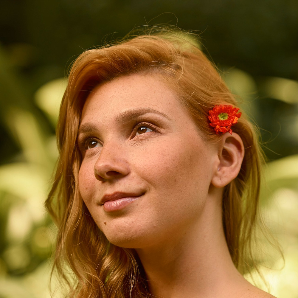 Young woman with a red flower in her hair looking up and smiling outdoors, representing confidence in birth control choices