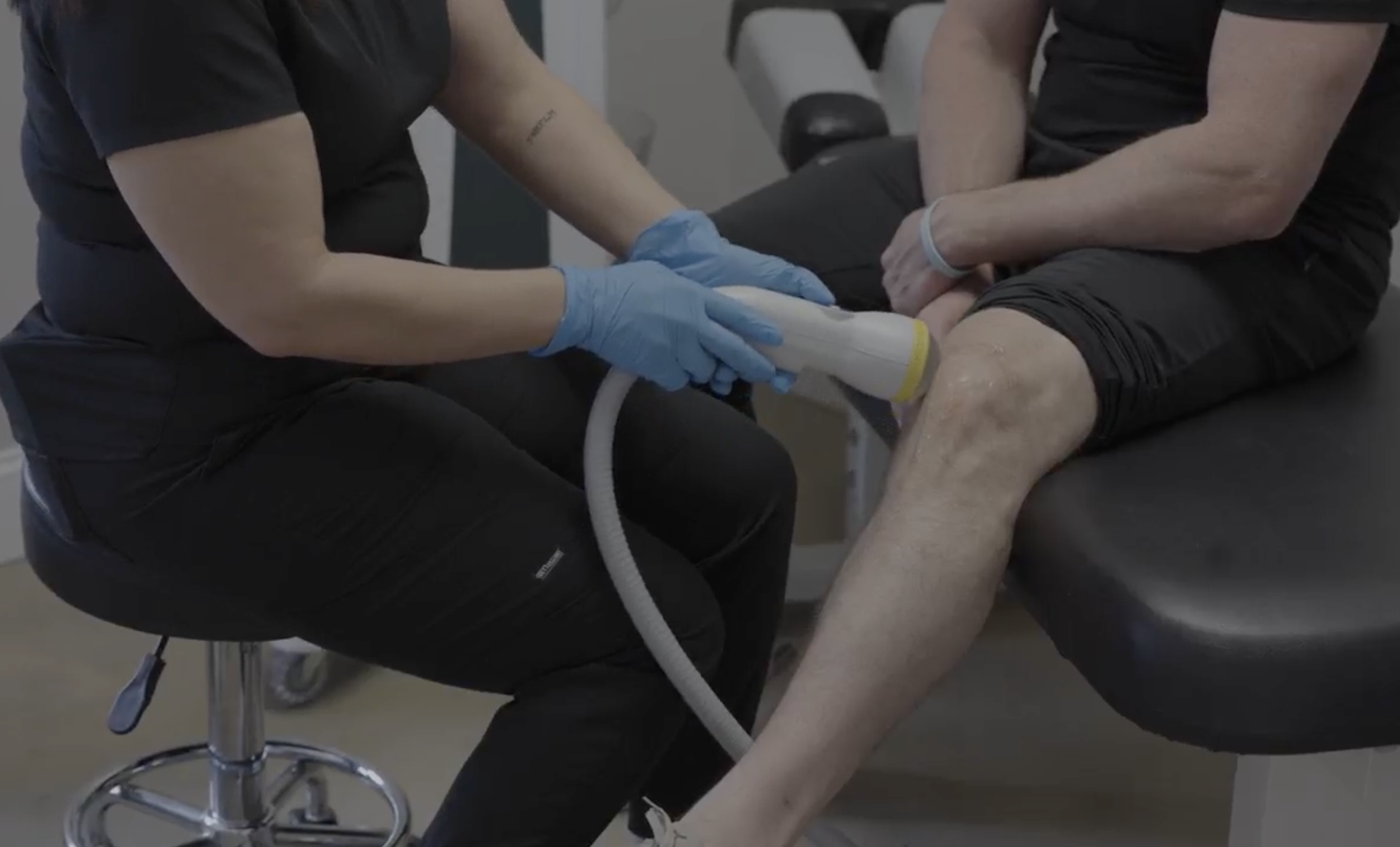 Young man in a gym gripping his shoulder with a pained expression, hinting at a sports injury or muscular discomfort, showed here as a great example of the patient who would do well with shockwave therapy.