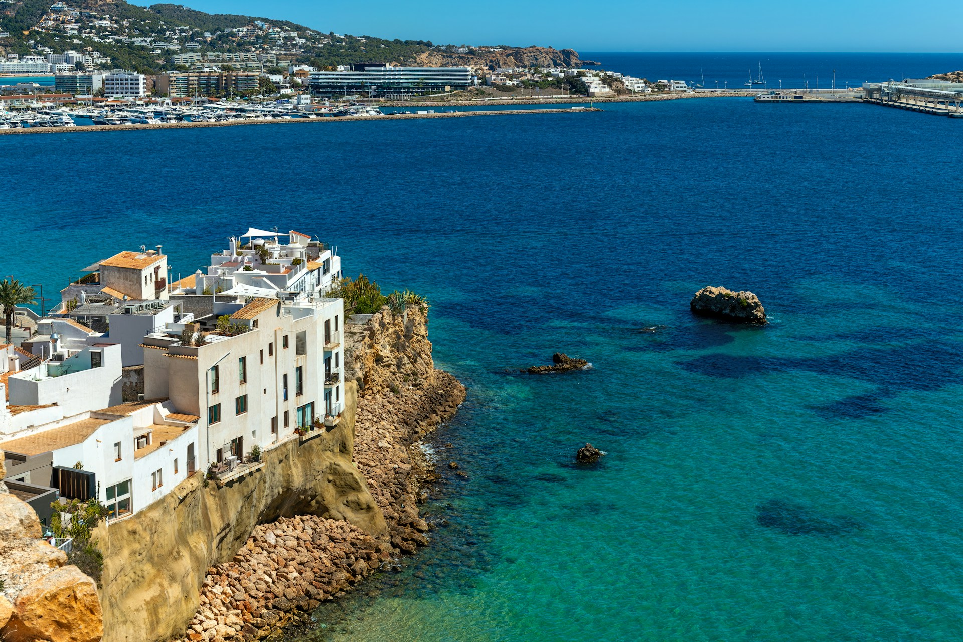 A scenic view of a beautiful beach with the city of Ibiza in the background under a clear blue sky.