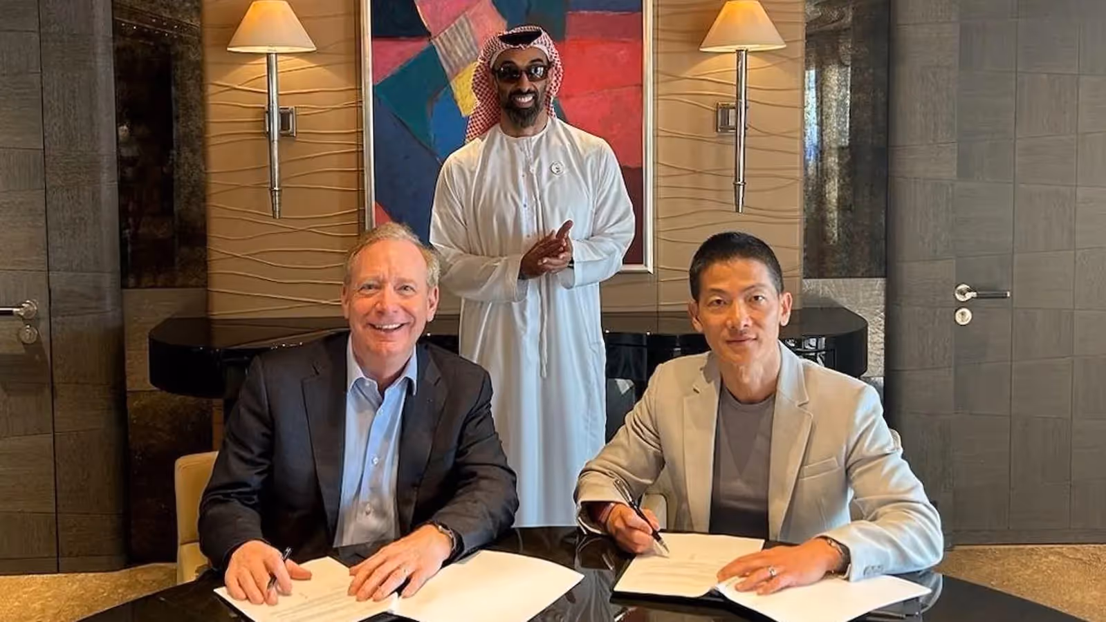 Brad Smith and Peng Xiao signing partnership agreement with UAE official standing behind, modern office background