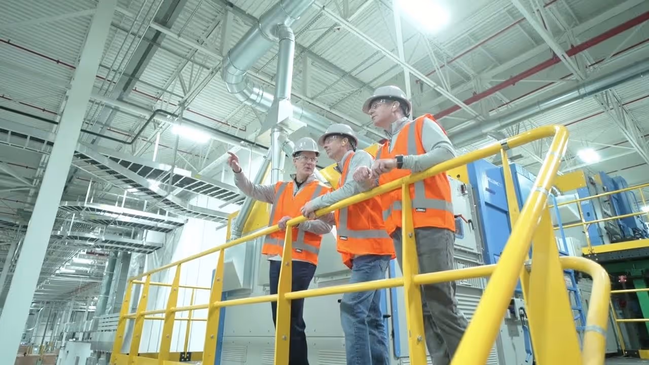Engineers in orange safety vests inspecting modern industrial equipment on elevated walkway inside factory