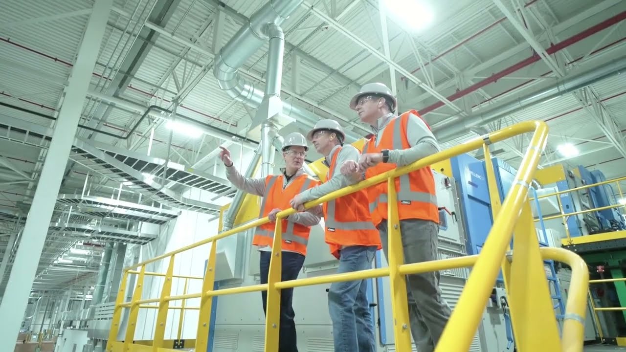 Engineers in orange safety vests inspecting modern industrial equipment on elevated walkway inside factory