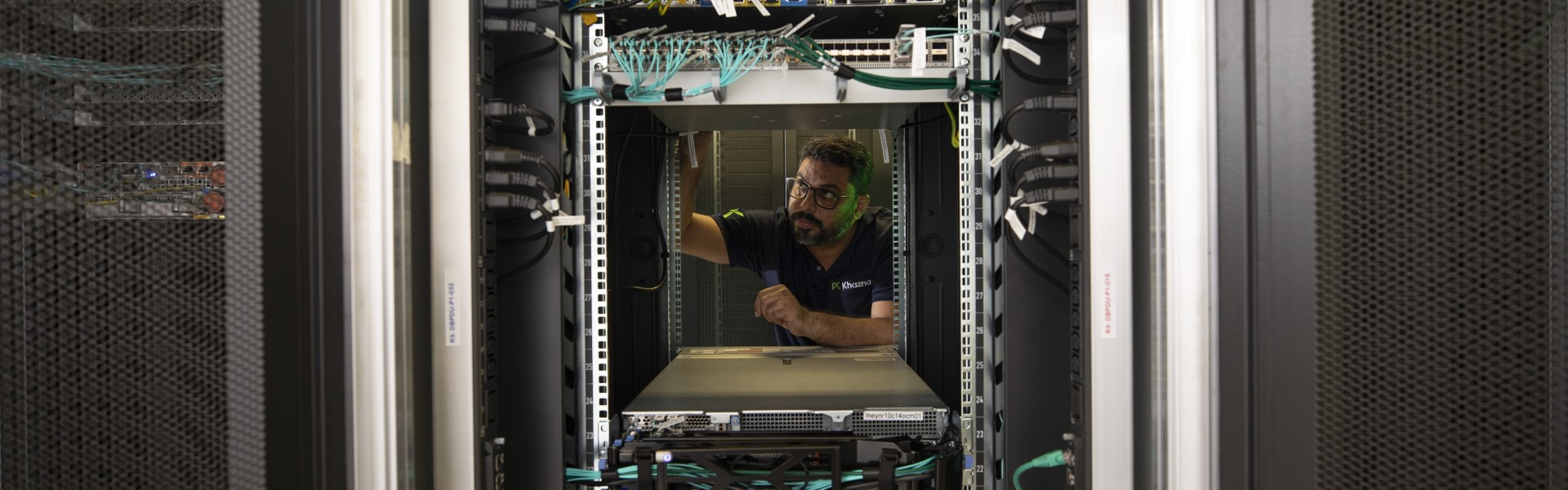 Technician working inside data center server rack managing network cables and equipment