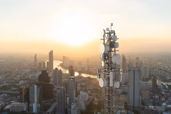 5G telecommunications tower overlooking a city skyline at sunset, representing global IoT connectivity infrastructure