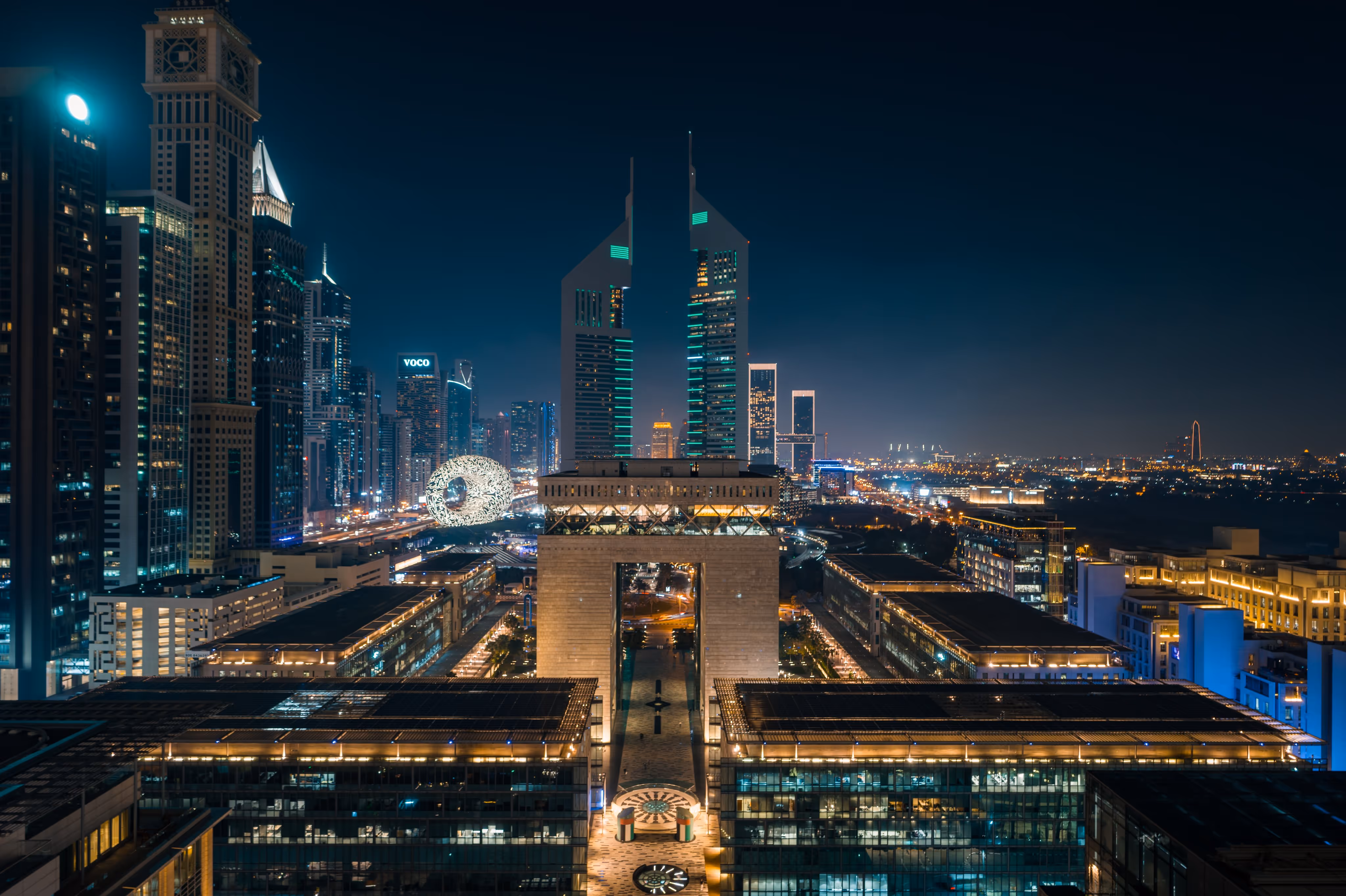 Nighttime view of Dubai International Financial Centre (DIFC) with illuminated skyscrapers and the Museum of the Future in the background.