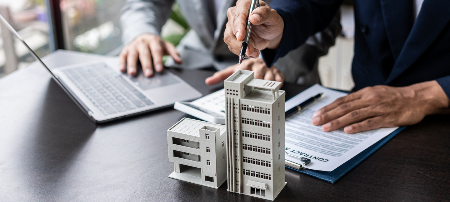 Investment professionals review financial documents beside a scale model of commercial buildings.