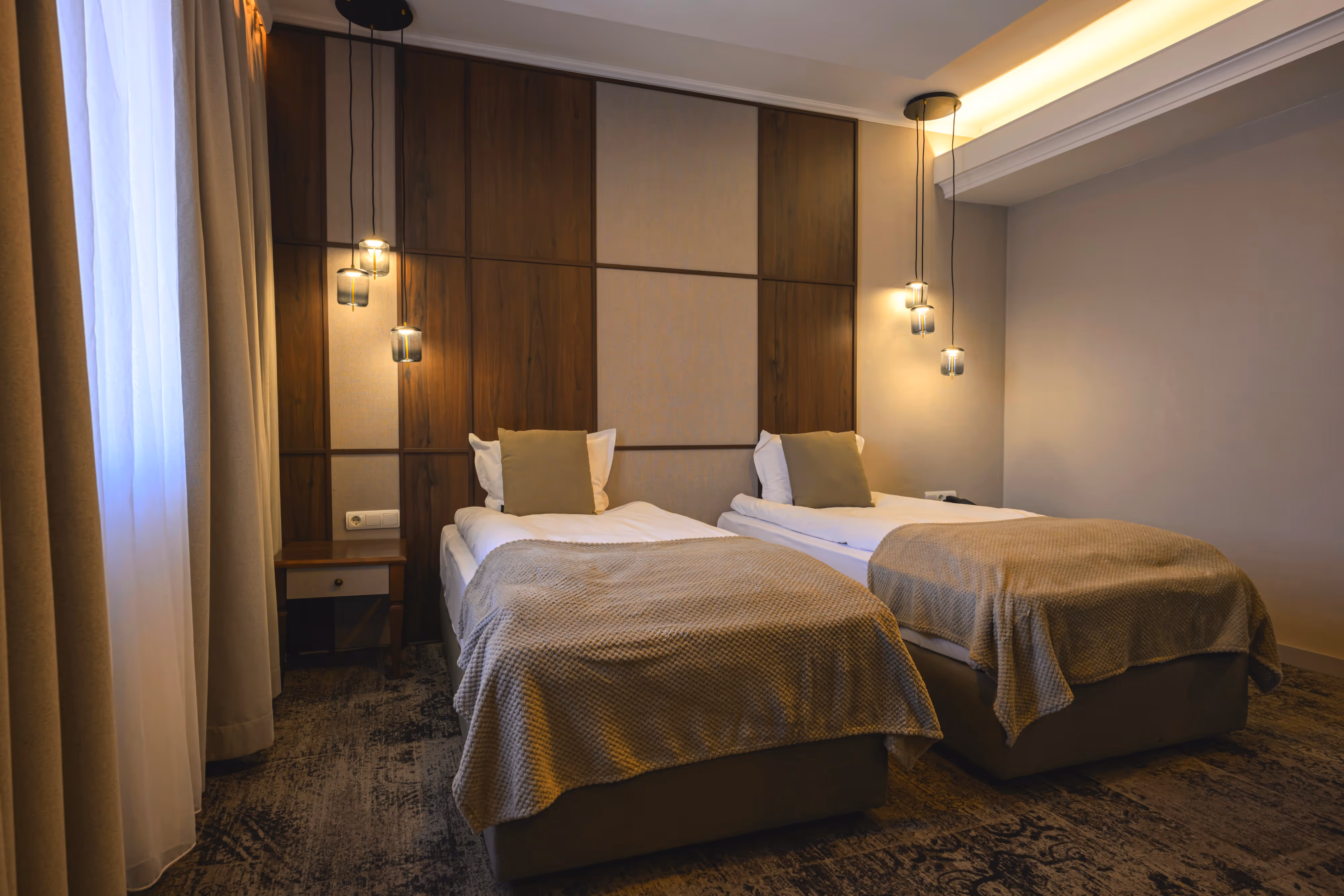 Двойна стая с изглед към Стария град – уютно обзаведена с две единични легла, стилни кафяви завеси с флорални мотиви и елегантни дървени мебели, създаващи топла и комфортна атмосфера.