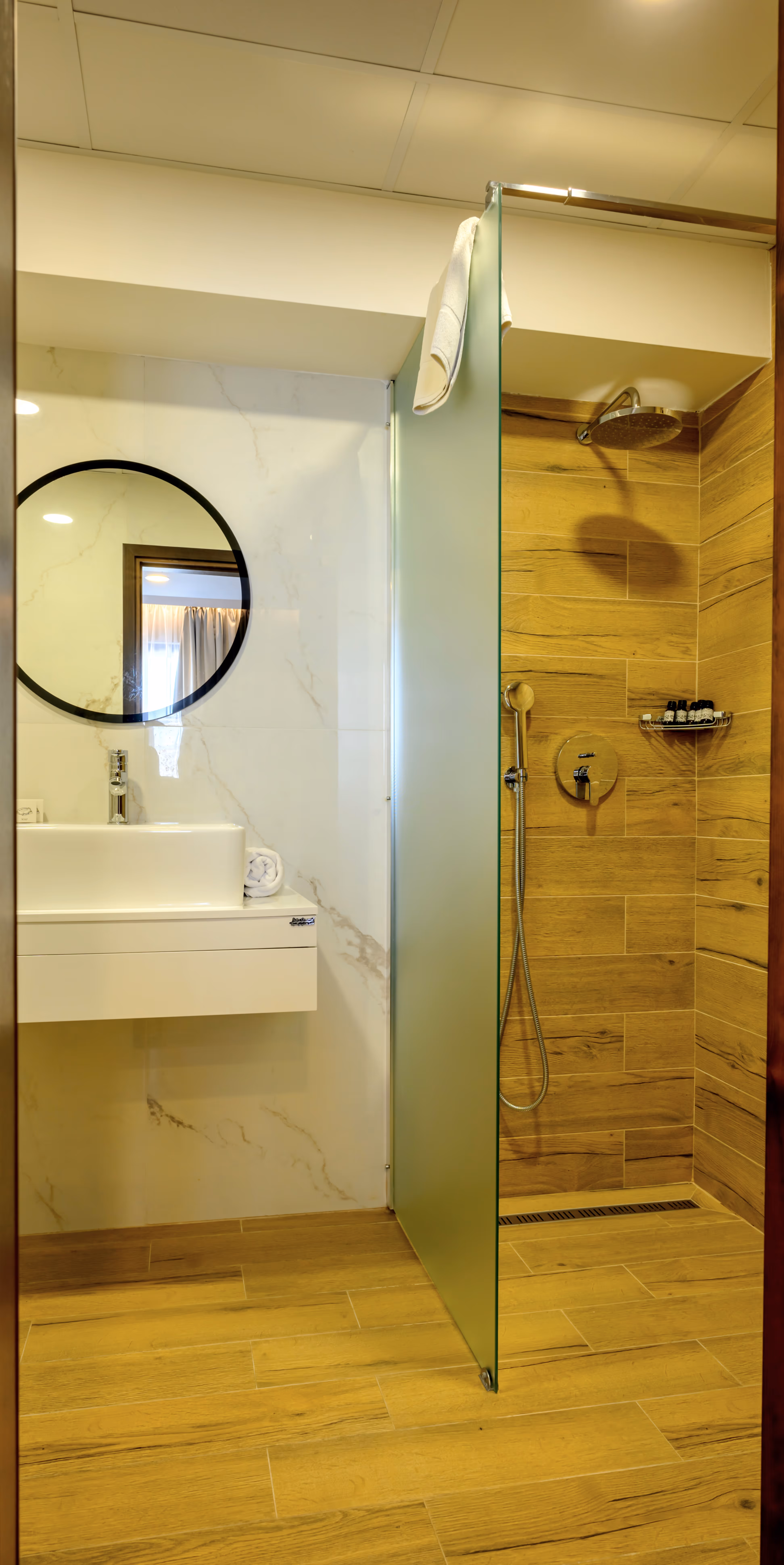 Светла баня с модерна бяла мивка, огледало, снежнобели кърпи с логото на хотела и малки декоративни акценти, създаващи уютна атмосфера.