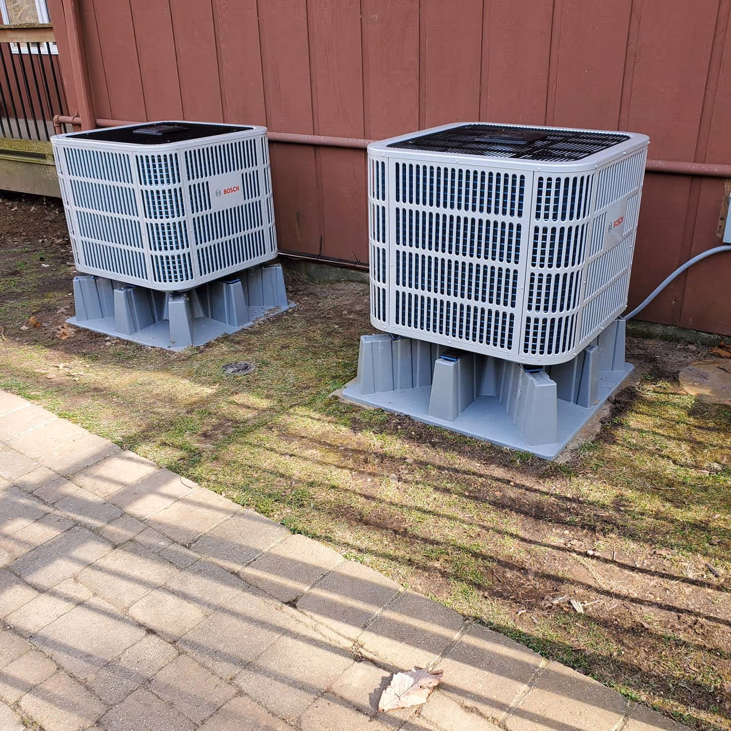 Two Bosch air conditioning units on concrete stands near red building