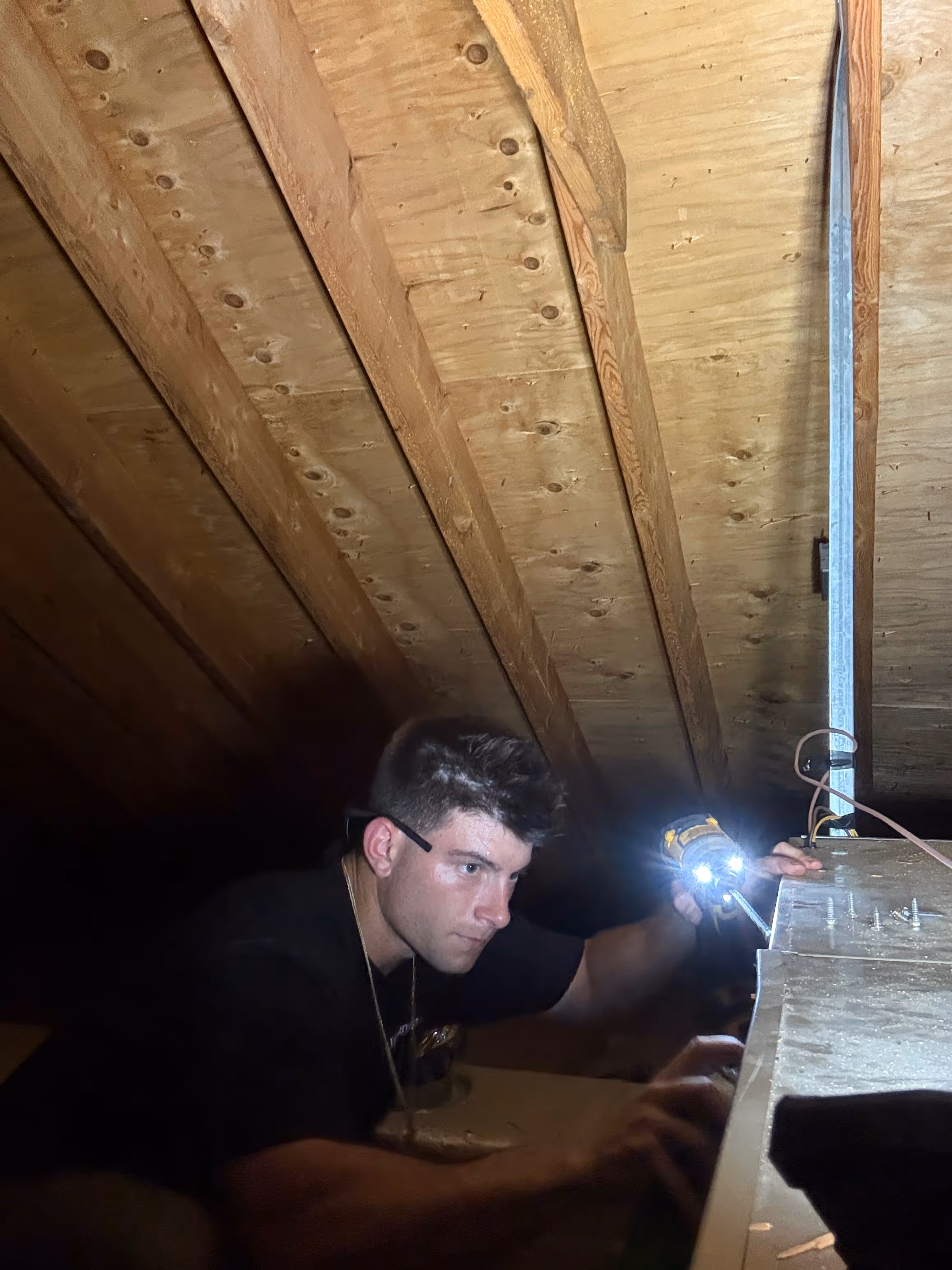 Person with flashlight working in dark wooden attic or crawl space