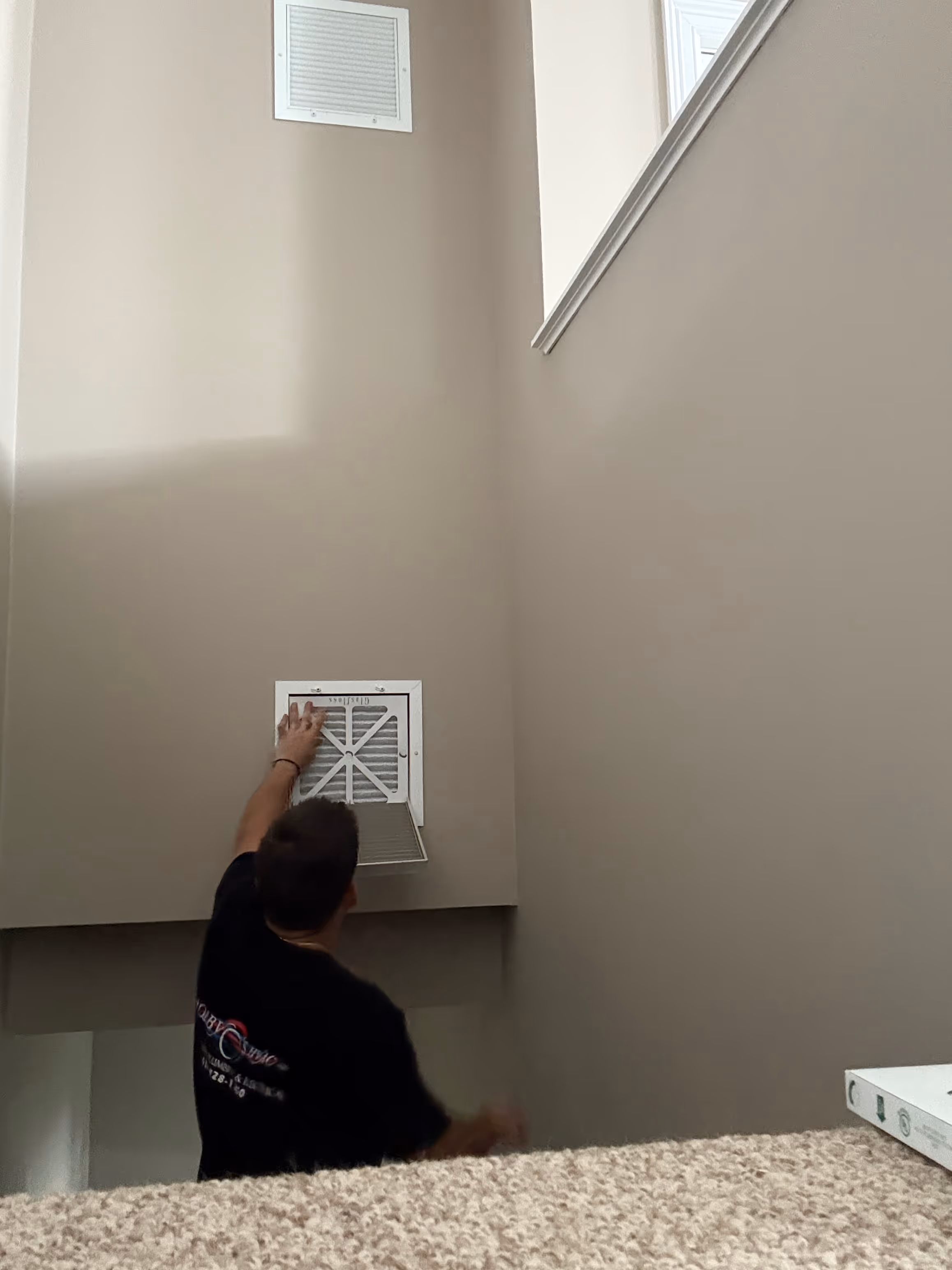 Person adjusting air vent on neutral-colored wall with carpeted floor