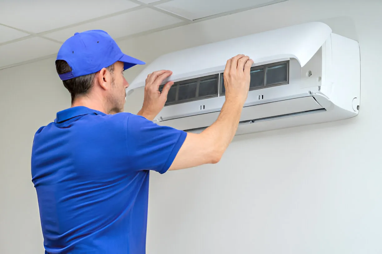 Technician in blue uniform checking and maintaining air conditioning unit