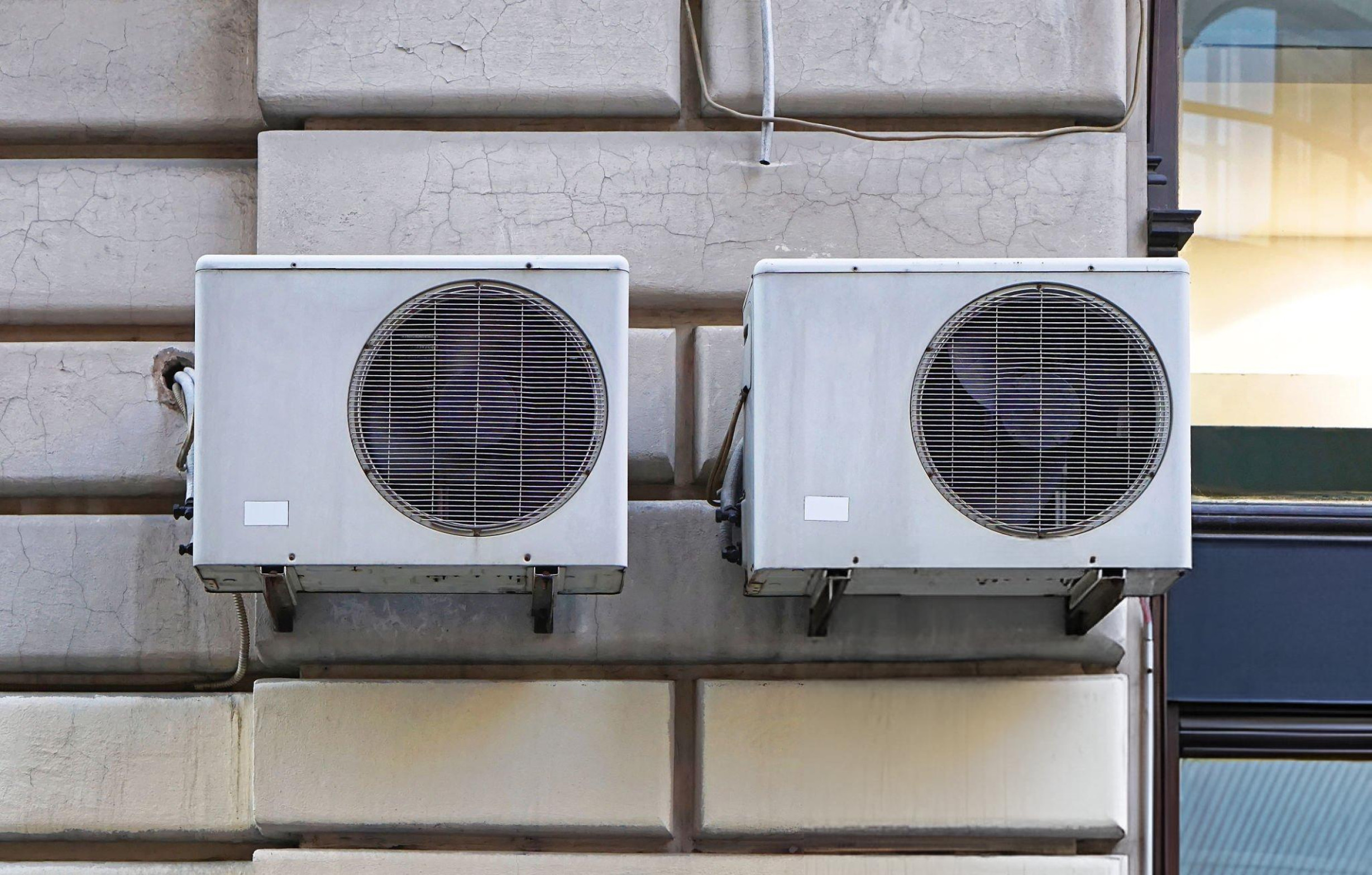 Two white air conditioning units mounted on a weathered concrete wall