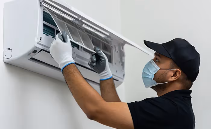 Technician in mask and gloves repairing wall-mounted air conditioning unit