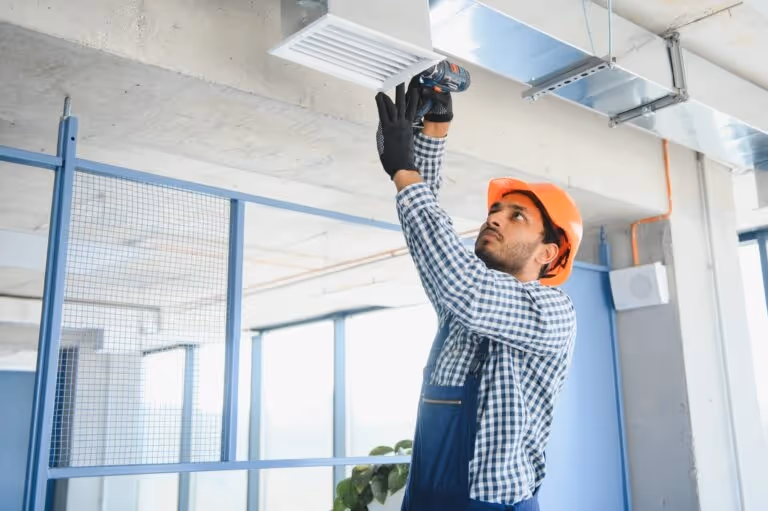 Worker in hard hat installing air vent with power drill in building