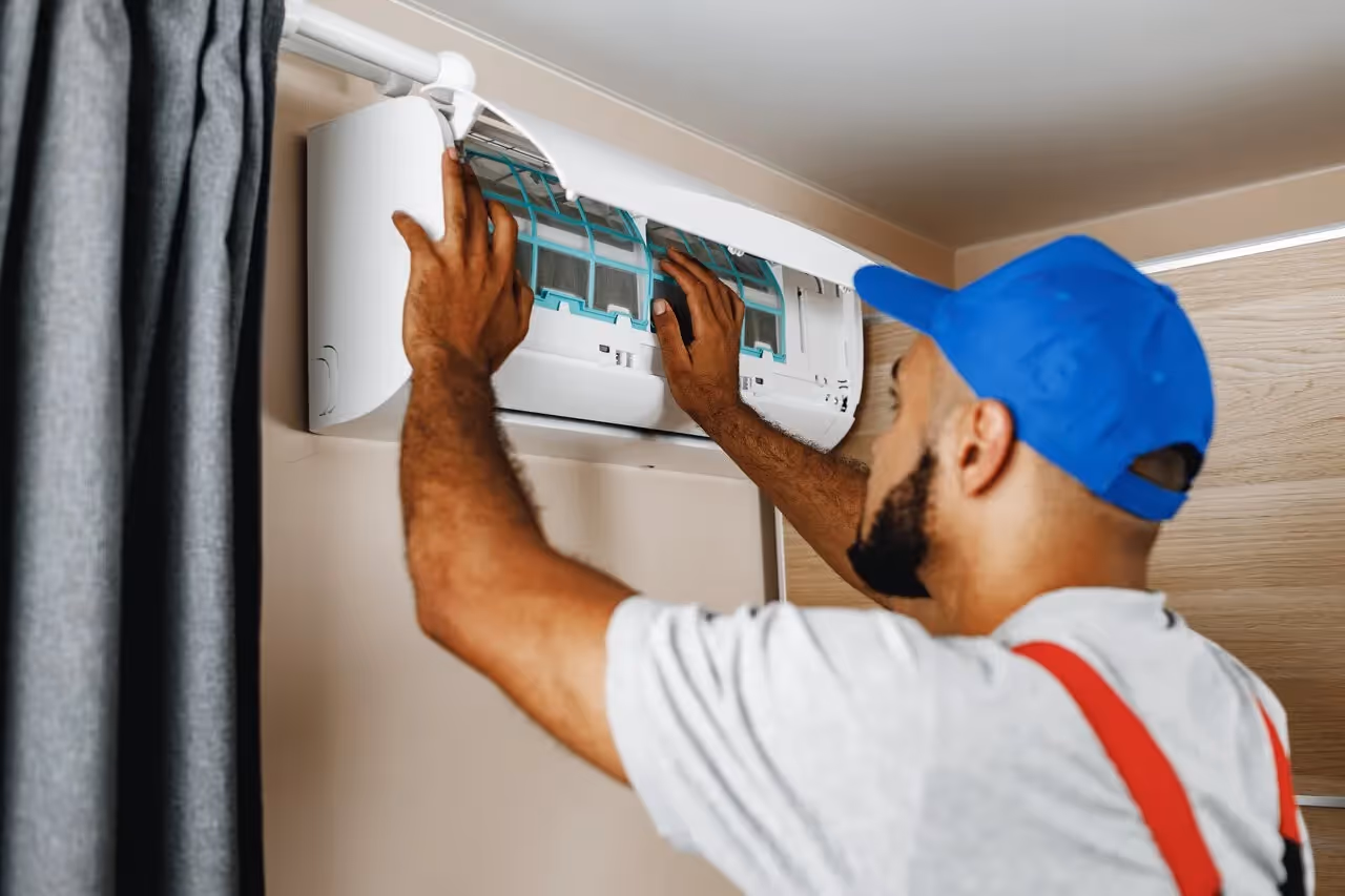 Technician in blue cap repairing air conditioning unit indoors