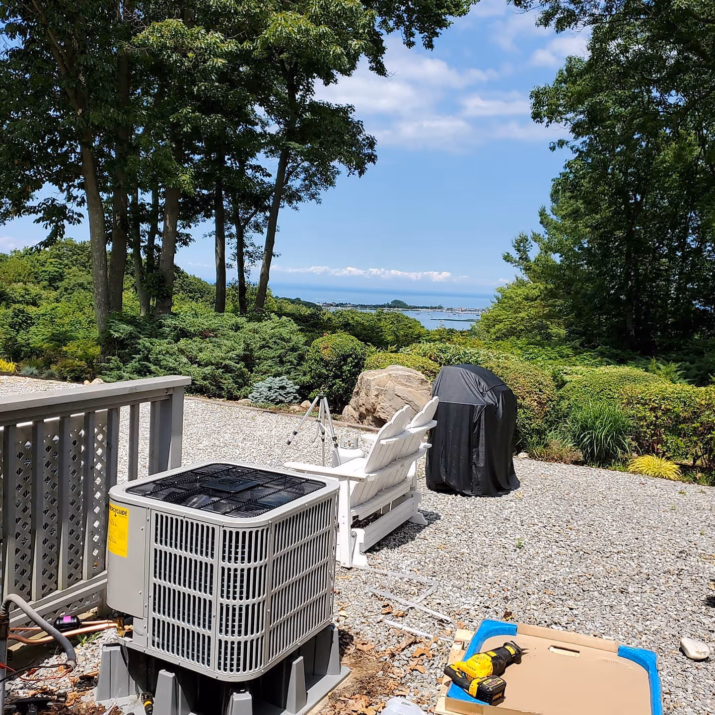 Air conditioning unit on gravel with ocean and trees in background