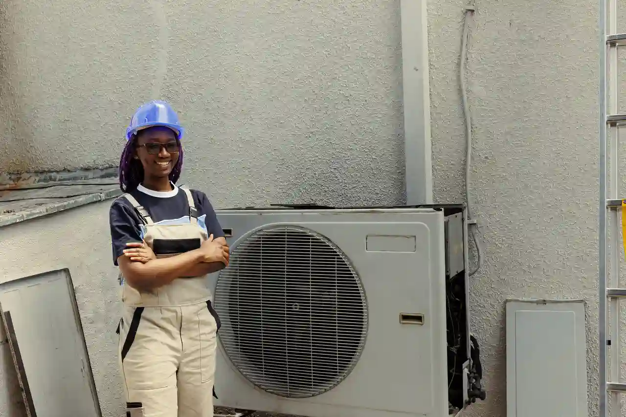 Smiling technician in blue hard hat standing near air conditioning unit