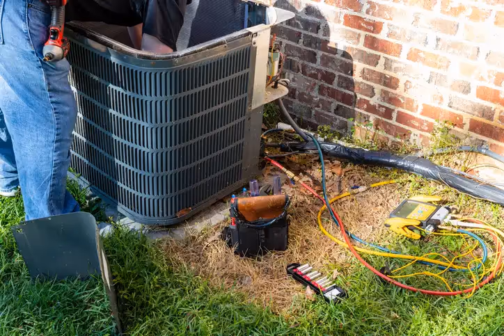 HVAC technician repairing air conditioning unit with tools outside brick wall