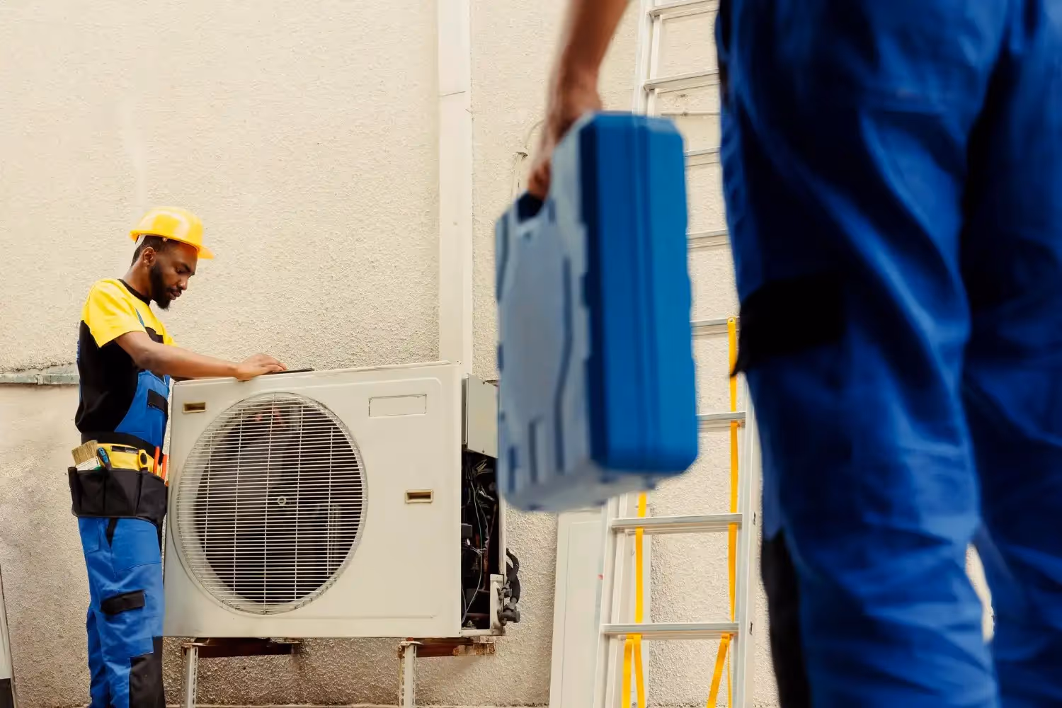 Technician in hard hat and blue uniform repairing an air conditioning unit