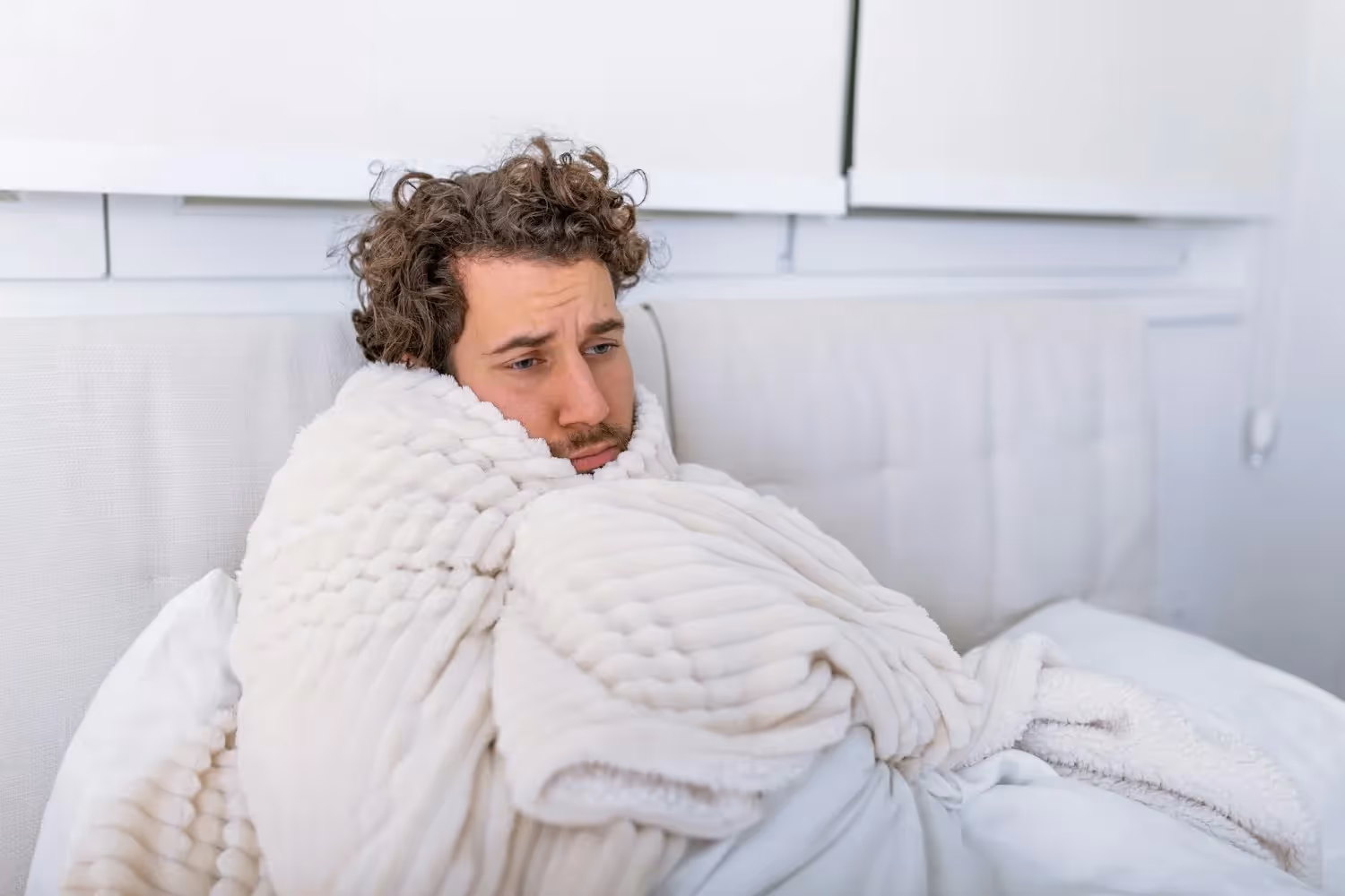 Curly-haired person looking unwell, wrapped in a white blanket