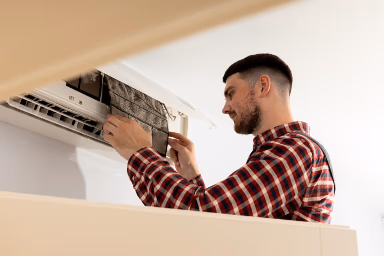 Technician in plaid shirt repairing and cleaning wall-mounted air conditioner