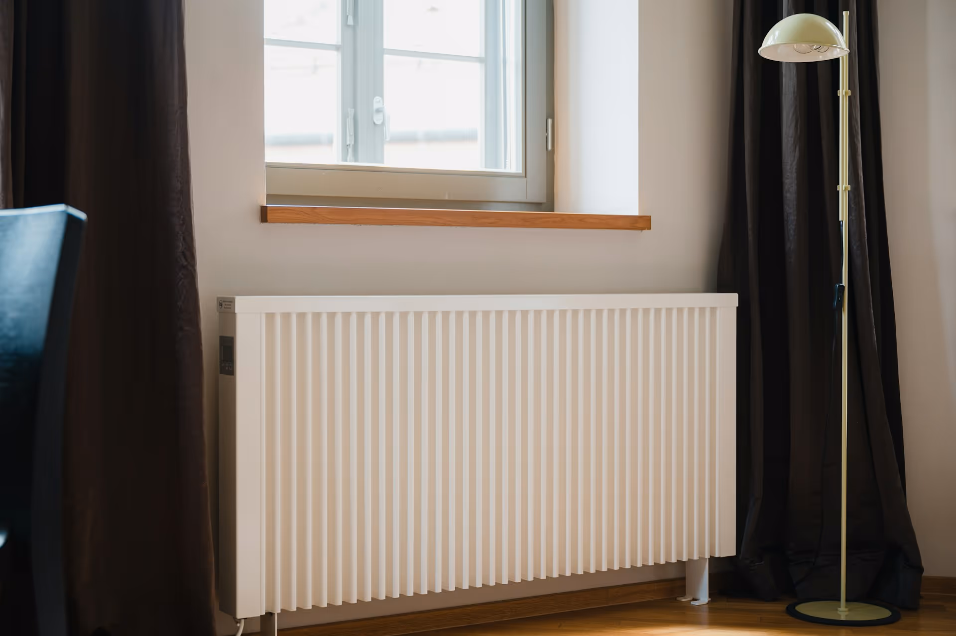 White radiator near window with black curtains and standing lamp