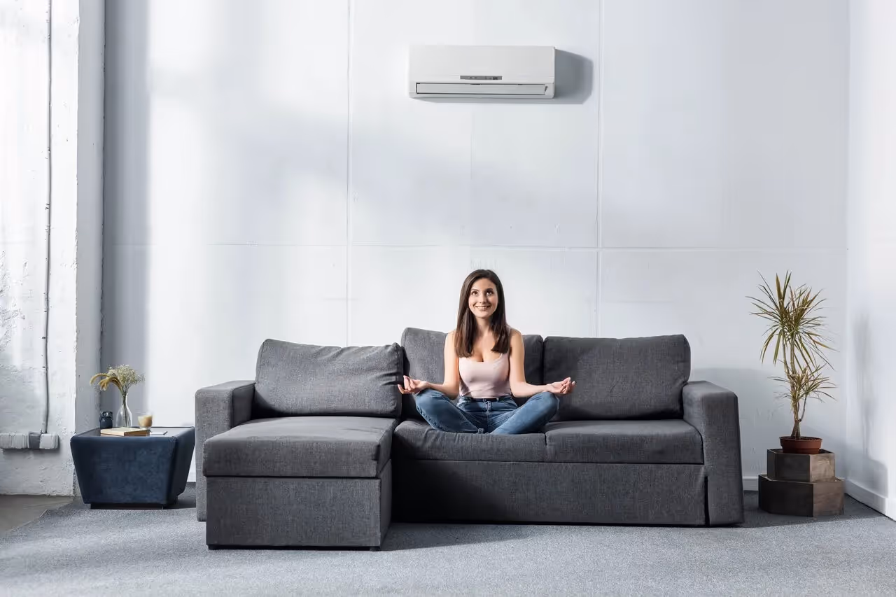 Woman meditating on gray couch in minimalist living room with air conditioner