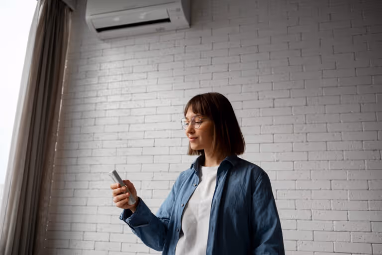 Person in blue jacket checks smartphone near white brick wall and window