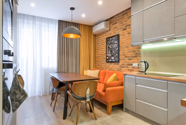 Modern compact kitchen and dining area with orange sofa and brick wall