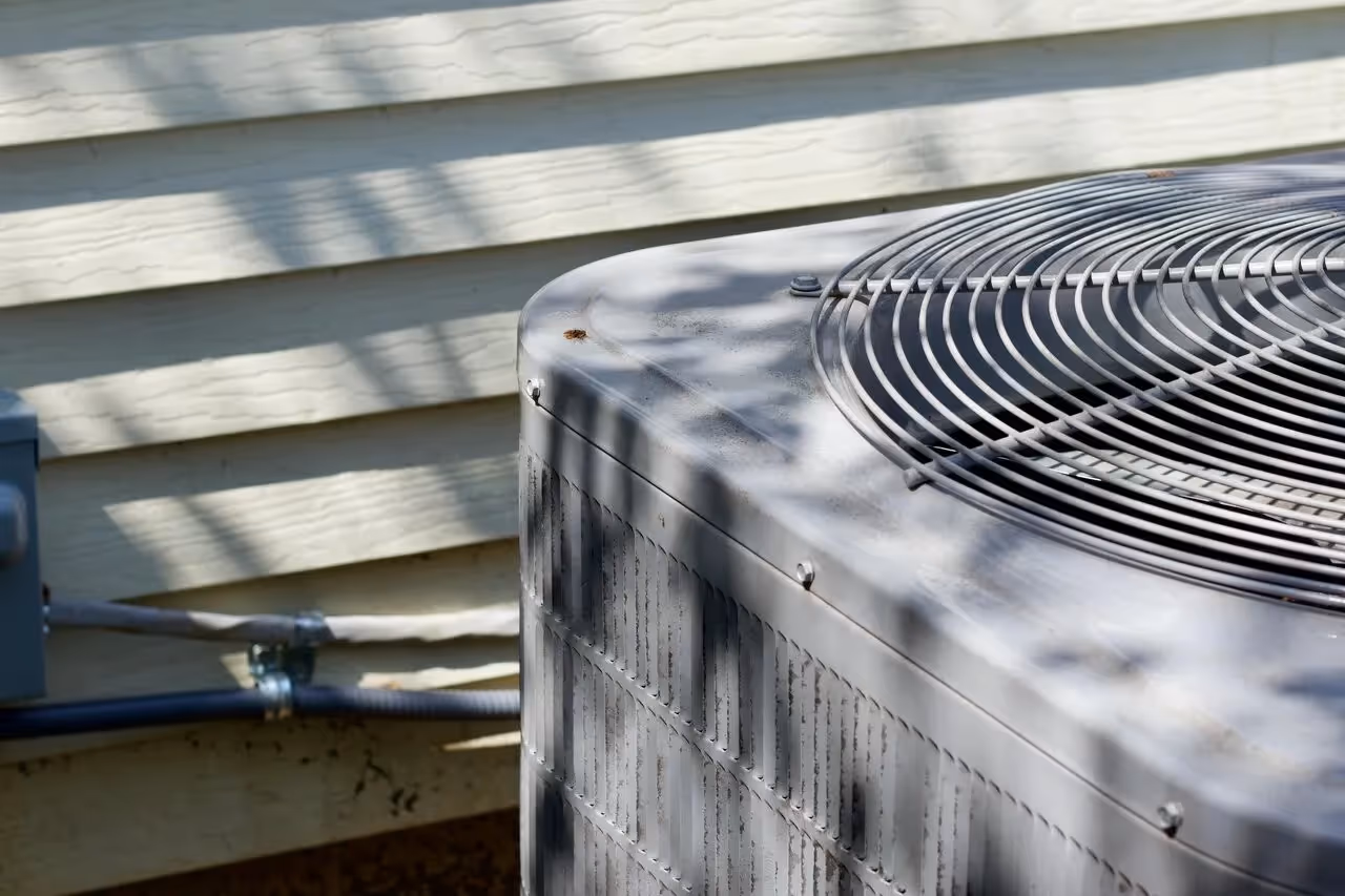 Outdoor air conditioning unit with circular fan, casting shadows on siding