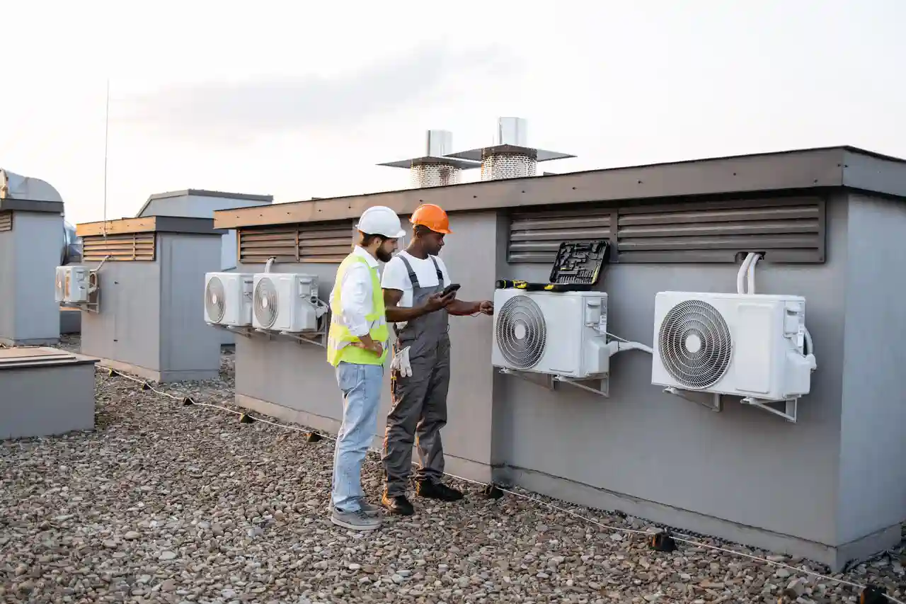 Two workers in safety gear inspecting air conditioning units on rooftop