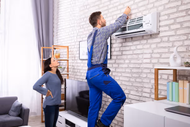 Technician installing air conditioning unit while customer watches in living room