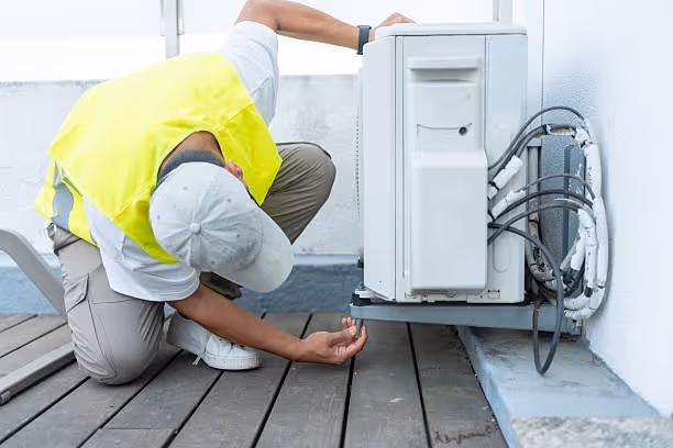 Technician in yellow vest repairing outdoor air conditioning unit