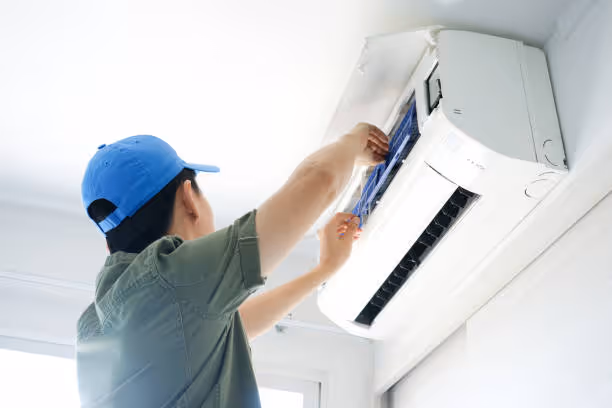 Technician in blue cap installing or repairing a white air conditioning unit