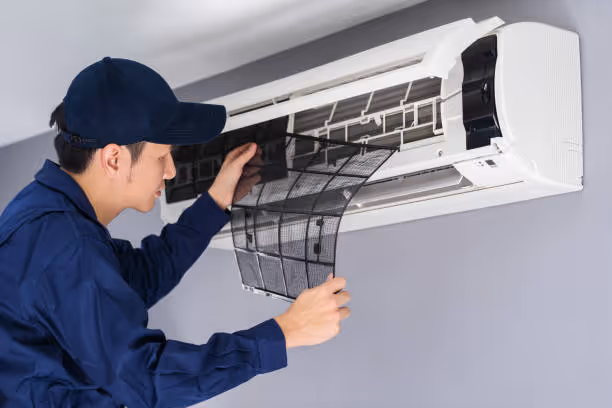 Technician in blue uniform checking and cleaning air conditioning unit