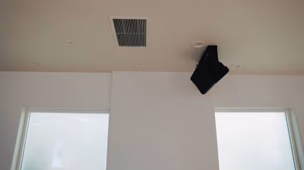 Black speaker mounted on white wall near air vent and windows