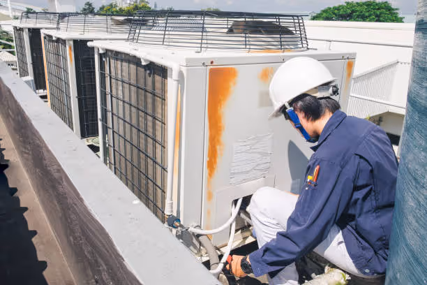 Technician in white hard hat inspecting rooftop air conditioning units