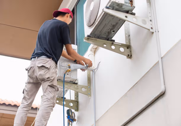 Technician installing air conditioning unit on exterior wall