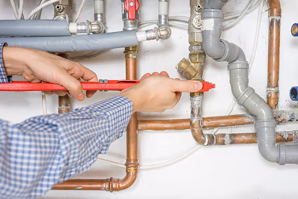 Plumber using red wrench to repair copper and PVC water pipes
