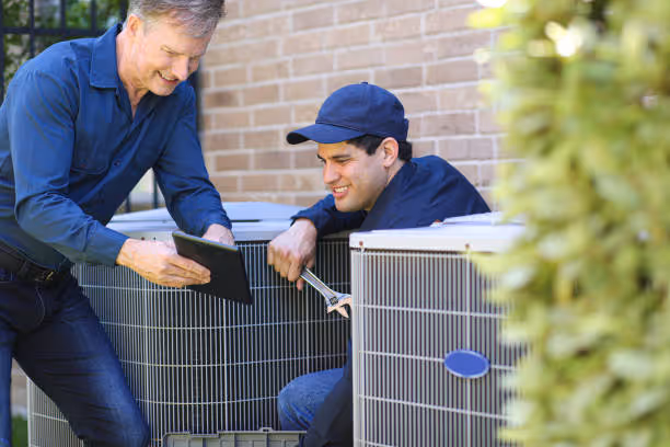 Two technicians repairing an air conditioning unit outside a building
