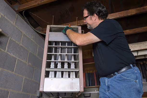 Man installing or repairing air conditioning unit in basement
