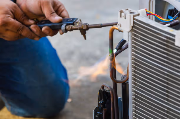 Technician using torch to repair air conditioner condenser unit