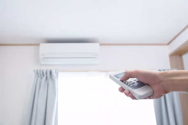 Hand holding remote control pointing at wall-mounted air conditioner