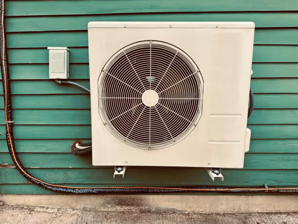 White air conditioning unit mounted on green wooden siding exterior wall