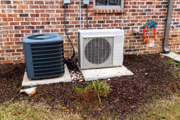 Two air conditioning units installed on concrete pad against brick wall