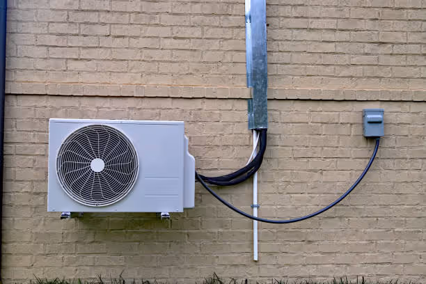 White air conditioning unit mounted on brick wall with electrical connections