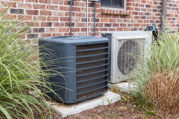 Two air conditioning units installed next to brick wall with surrounding grass