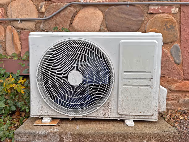 Air conditioning unit mounted on stone wall with plants nearby
